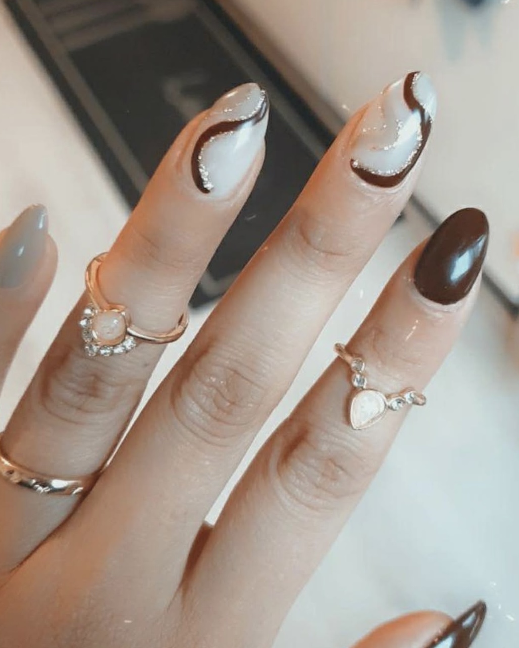 Nagels met een witte swirl en een bruine nagel, met ringen