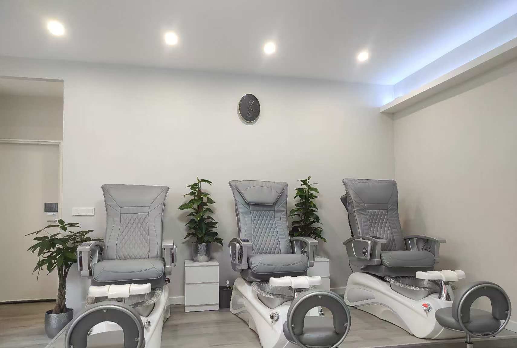 Drie grijze pedicurestoelen met massage en voetbaden, met planten ertussen